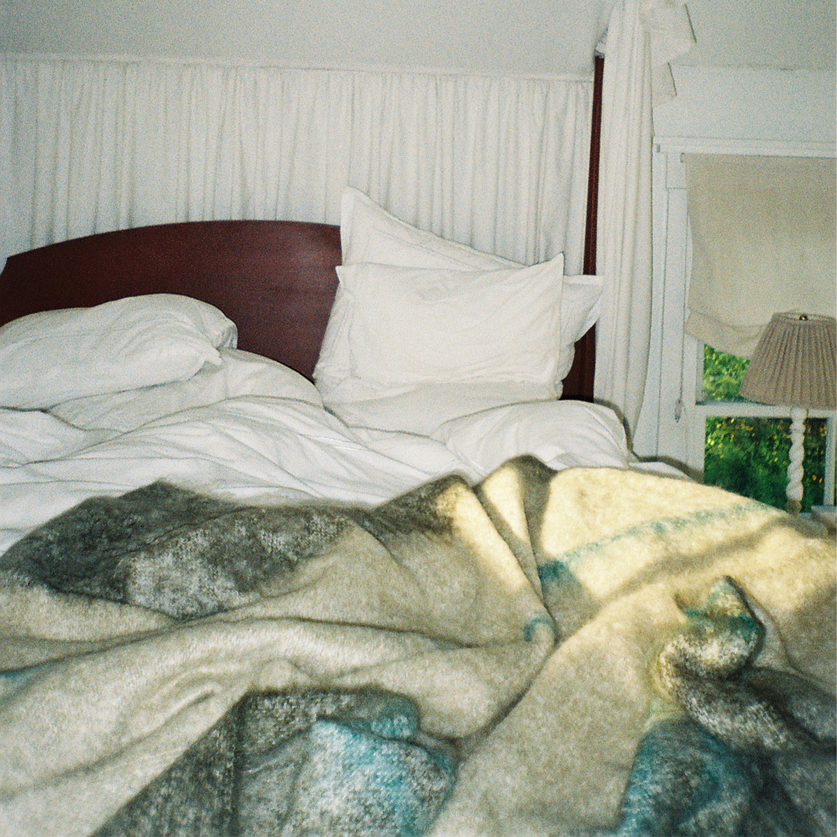 A bed with white bedding and pillows, featuring a dark wood headboard and a soft multicolor mohair blanket in the foreground, set in a softly lit bedroom.