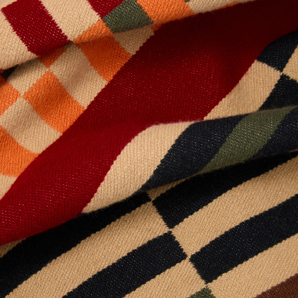 A close-up of a folded woven textile with a multicolor geometric pattern, showing cream, red, orange, green, and dark navy stripes and blocks.