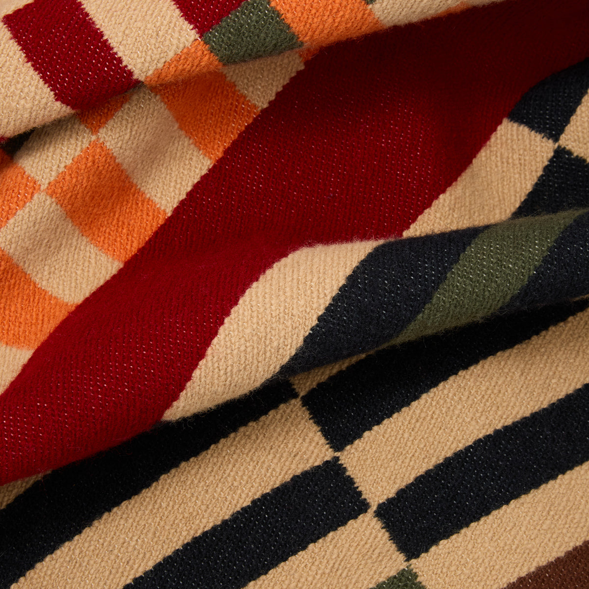 A close-up of a folded woven textile with a multicolor geometric pattern, showing cream, red, orange, green, and dark navy stripes and blocks.