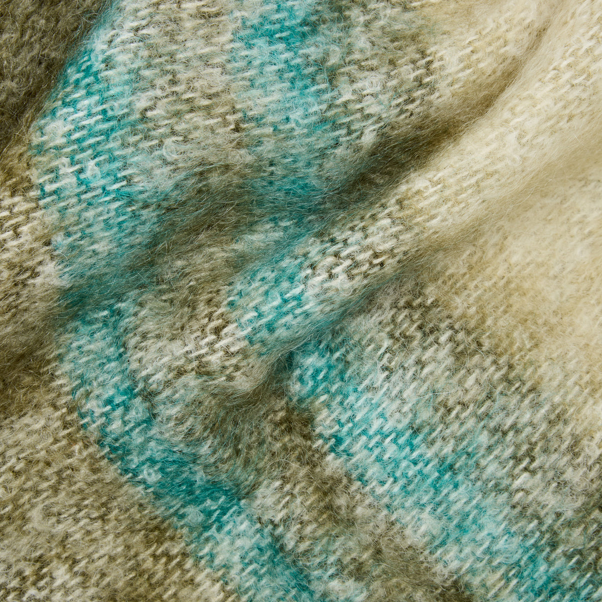 A close-up of a soft, textured knit fabric with a mottled pattern of teal blue, beige, and brown.